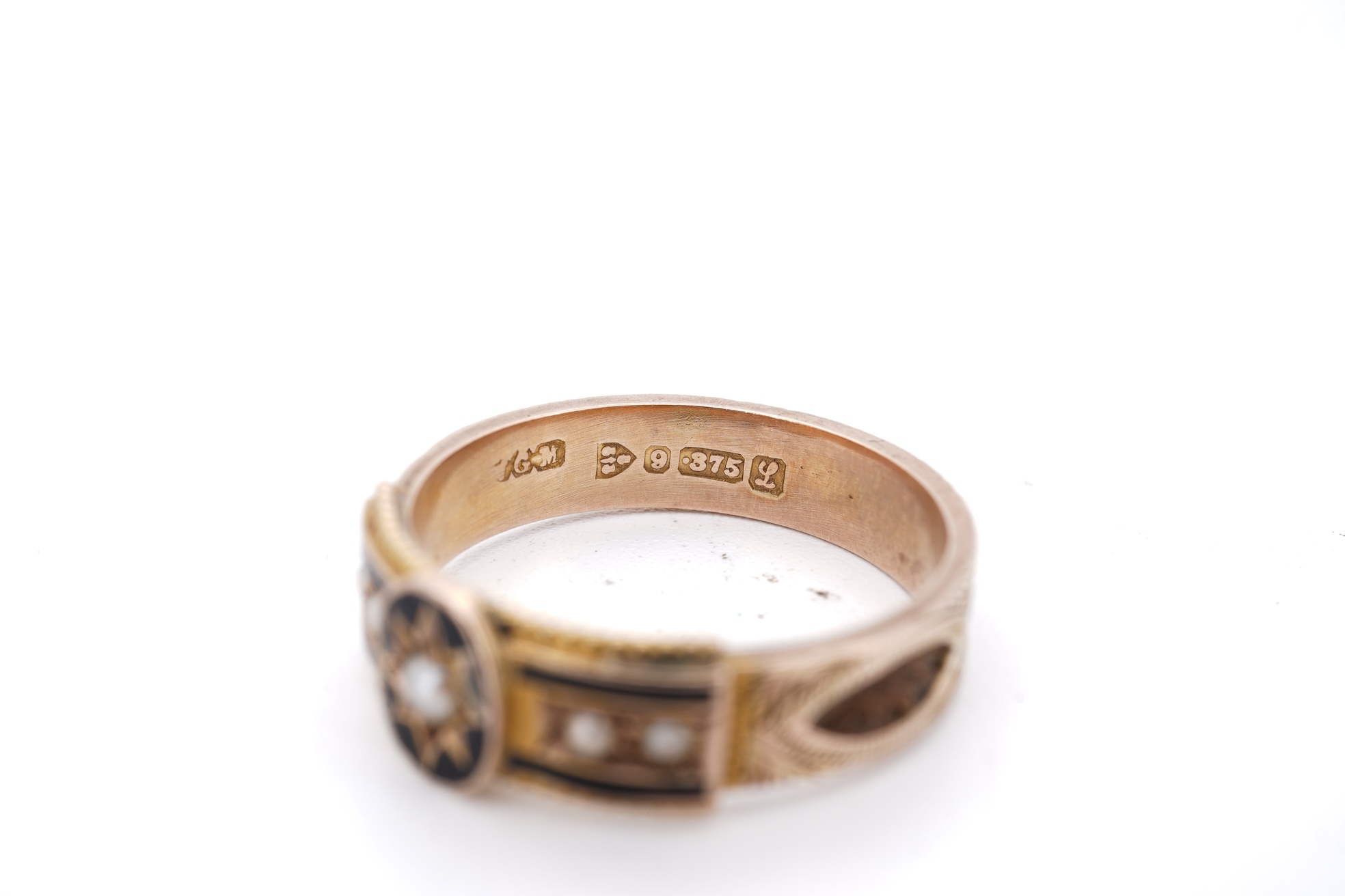 A George V 9ct gold, black enamel and seed pearl set mourning ring, the shank with panels of plaited hair, size O, gross weight 2.5 grams.